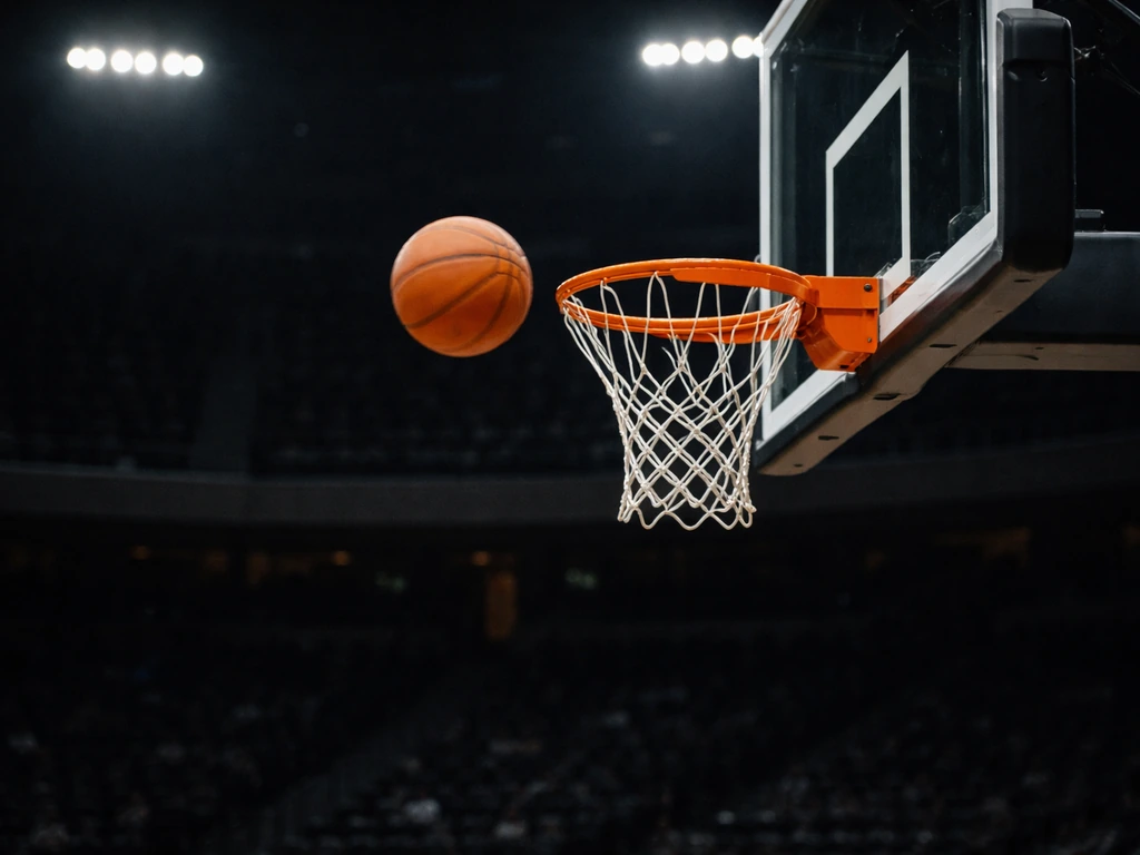 Orange basketball arcing toward the rim in a dim arena, hoop and net in view, no identifiable players.